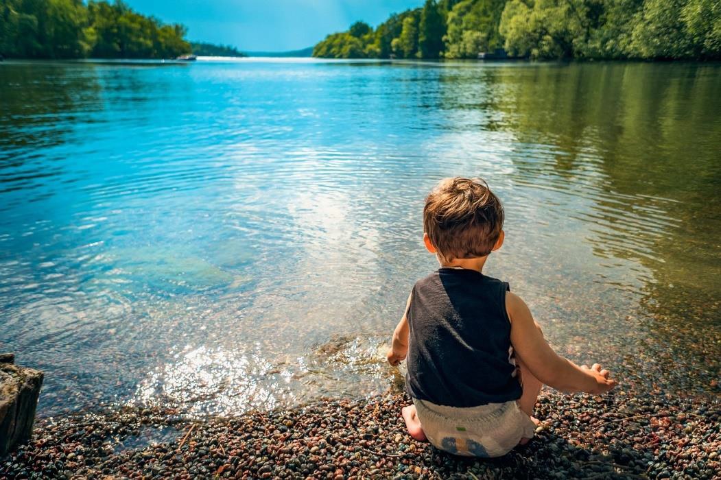 Ein kleiner Junge sitzt mit dem Wasser spielend an einem See